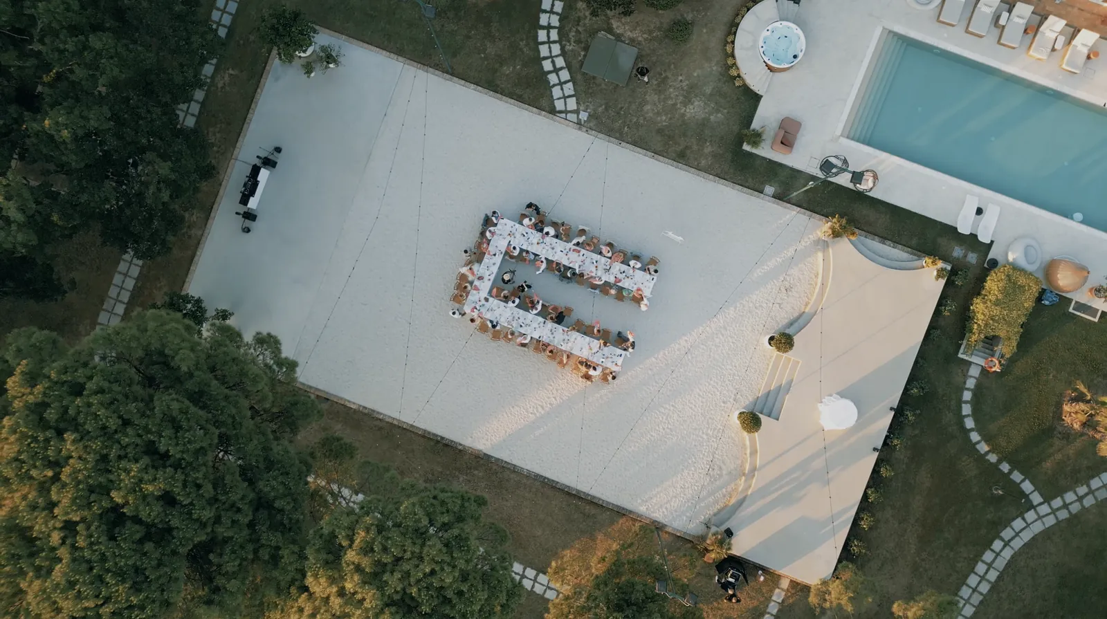 Top-down drone view of a U-shaped wedding table on the stage and dine area next to the pool