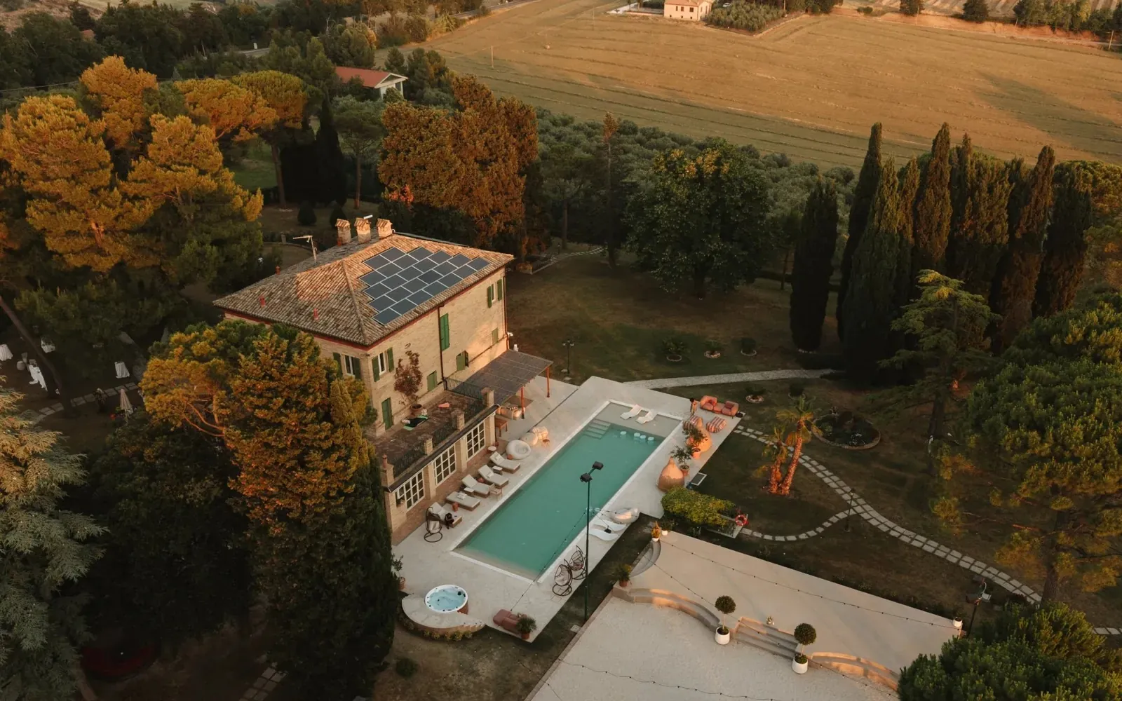 The villa and pool from above at golden hour, with the hills of Le Marche behind