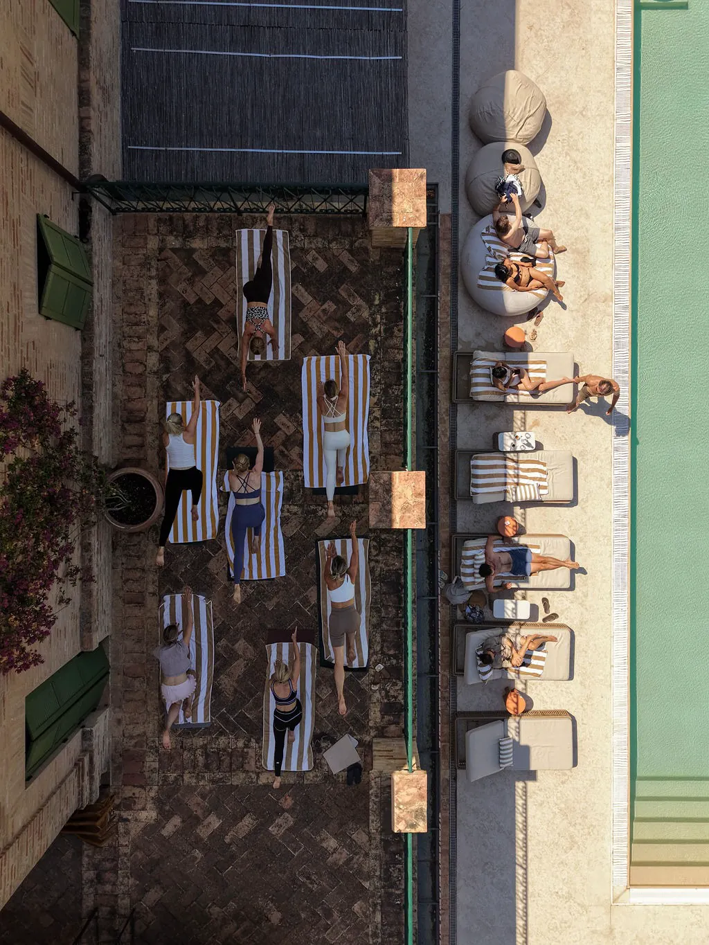 Drone view of a yoga class on the terrace beside the pool at Maniero, guests relaxing on the loungers